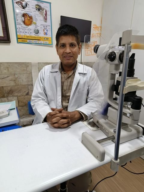 Dr. Gautam in a white coat, seated beside a slit lamp in his clinic
